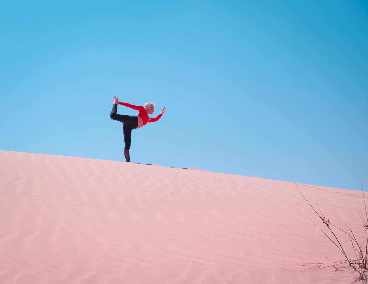 A woman practices yoga on sand dunes in Dubai, enjoying the clear blue sky and vast desert landscape.